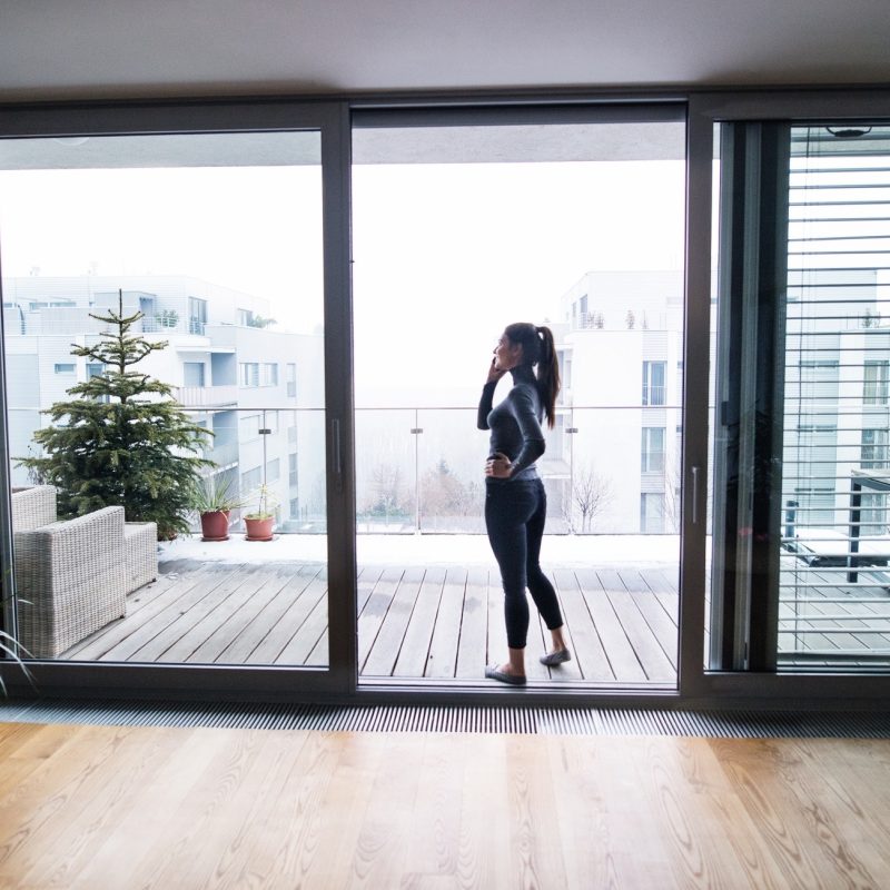 Woman by the window with smartphone, making a phone call.